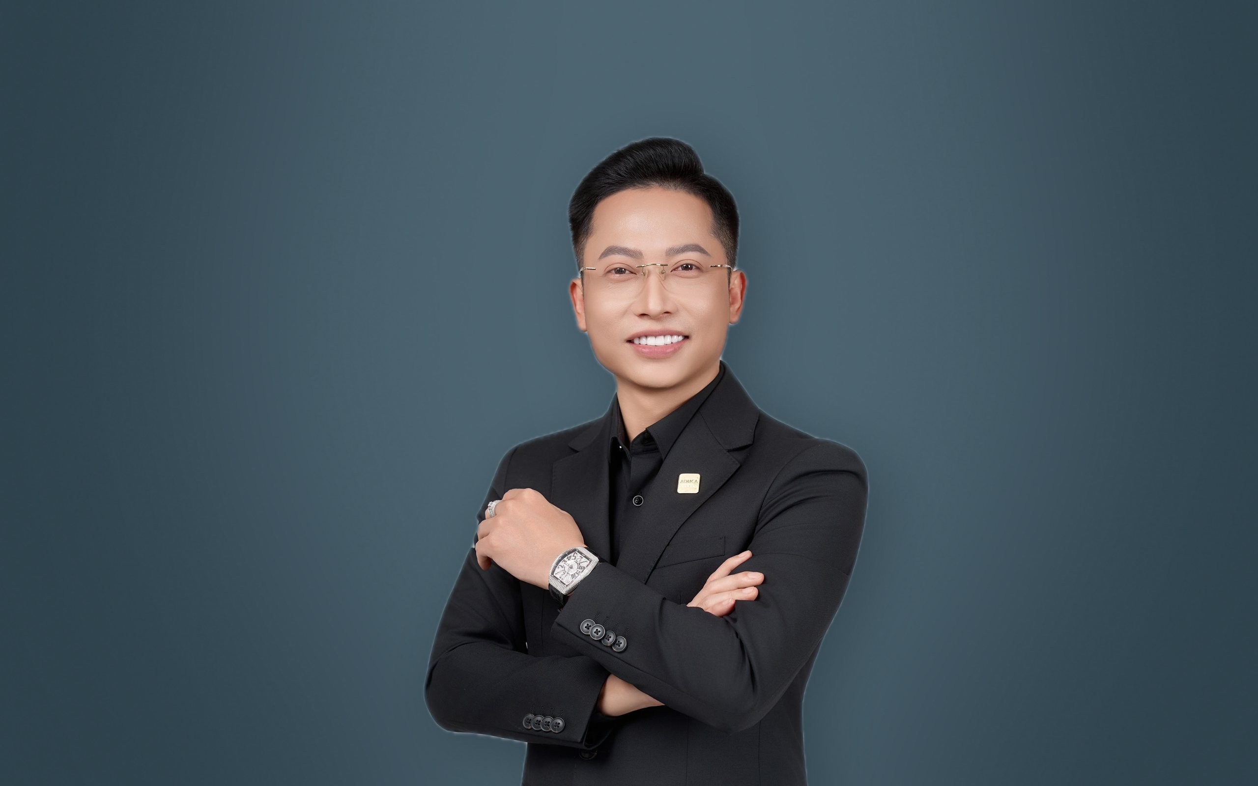 Nguyễn Đức, Chủ tịch Aduca Group, khoanh tay mỉm cười trước nền tường xanh đá